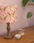 Lamp with a floral patterned shade on a wooden surface with a plant in the background
