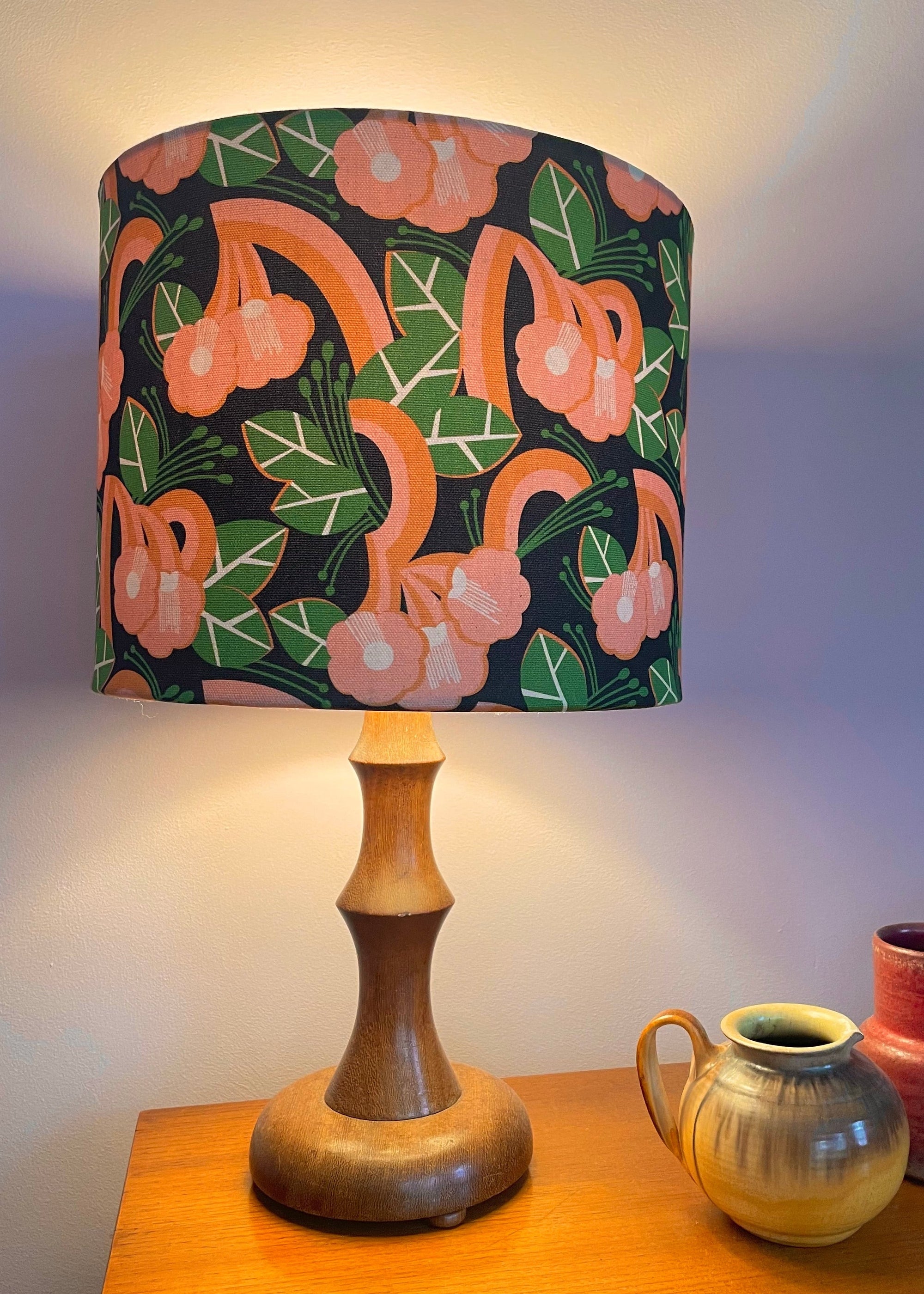 Lamp with a floral shade on a wooden table with two small vases.