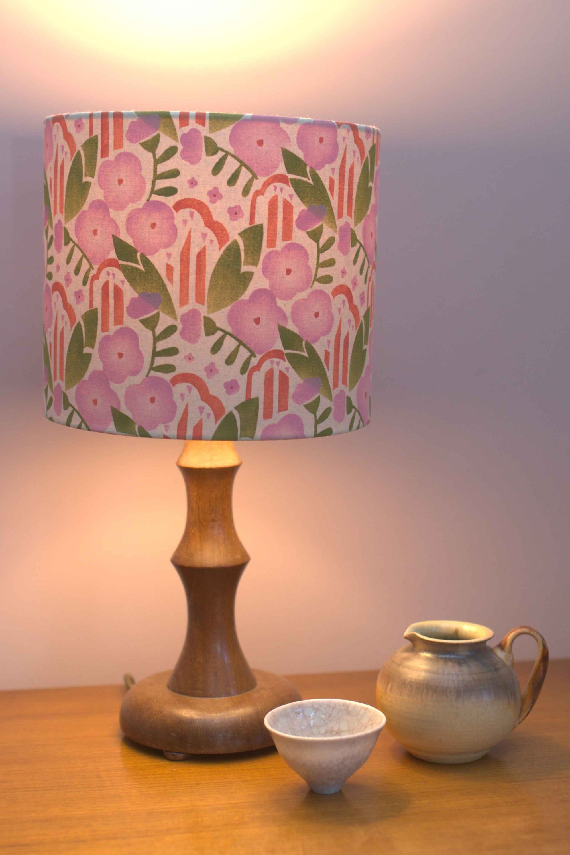 Lamp with a floral patterned shade on a wooden table with two ceramic items.