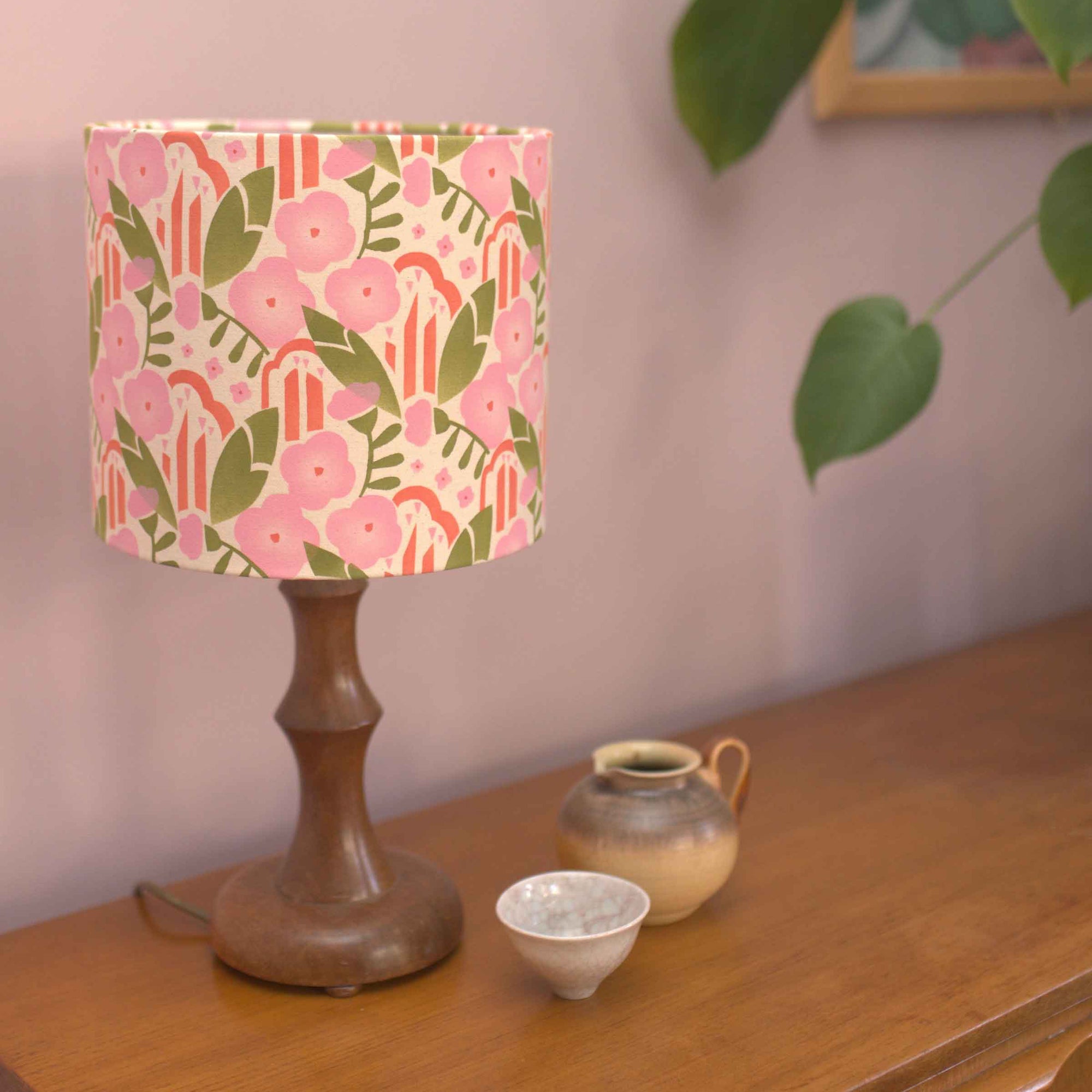 Lamp with a floral patterned shade on a wooden surface with a plant in the background
